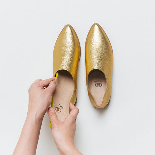Hands inserting replacement footbed insoles into a pair of Gold leather babouche sneakers from Babos.